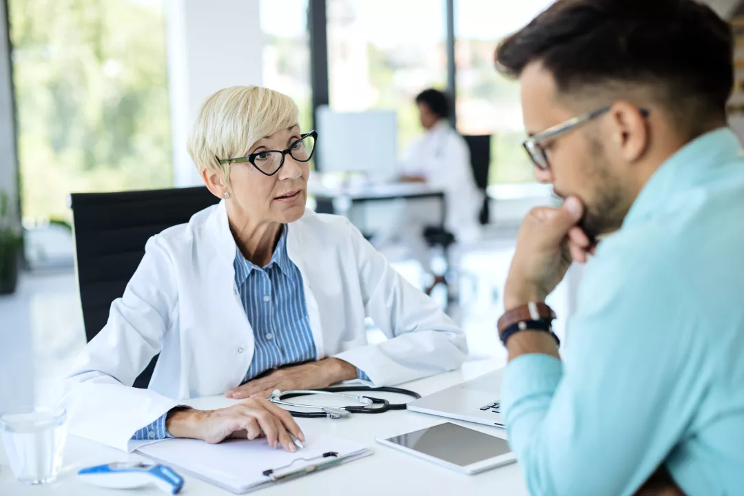 A doctor in a white coat consults with a patient in a modern medical office. The image underscores the importance of professional healthcare interactions and the role of doctors in patient care.