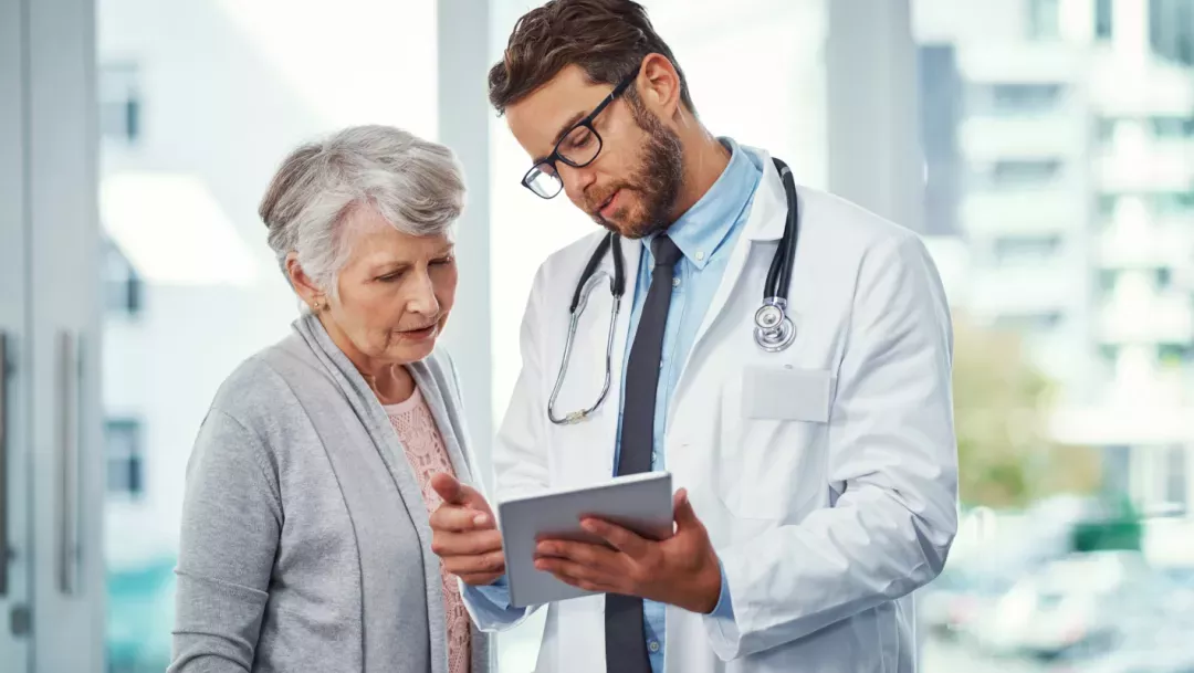 Médico atendendo paciente idosa, mostrando um documento.