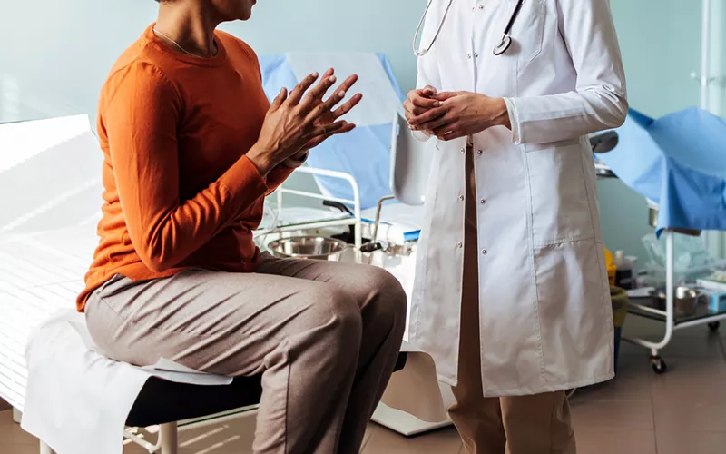 Consulta médica em consultório Paciente sentada conversando com profissional de saúde de jaleco em um consultório, com equipamentos ao fundo