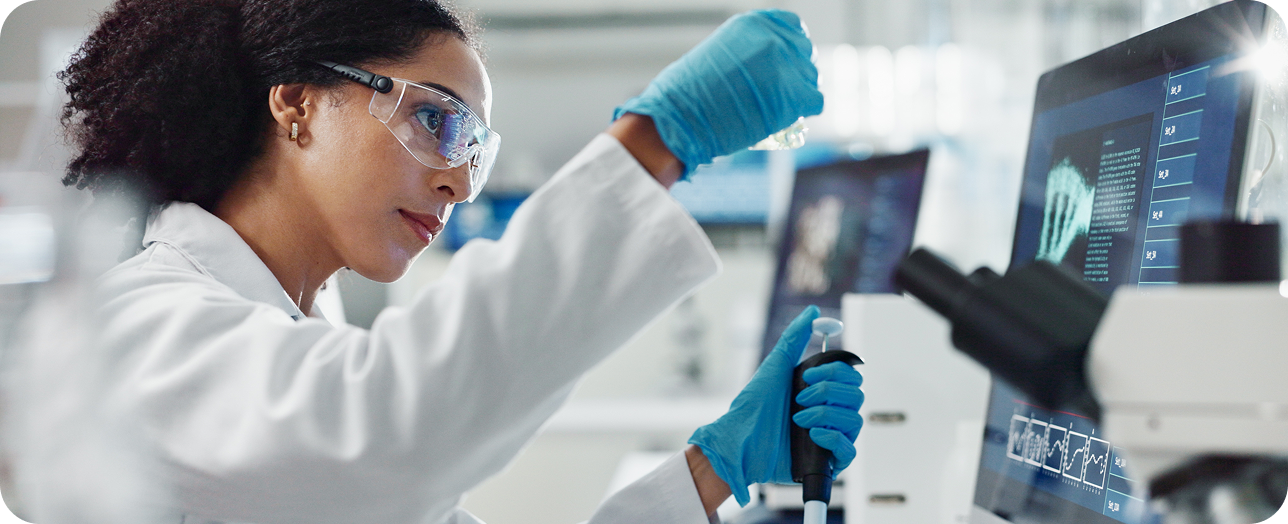 Mujer con bata de laboratorio trabajando en una computadora en un entorno de investigación.