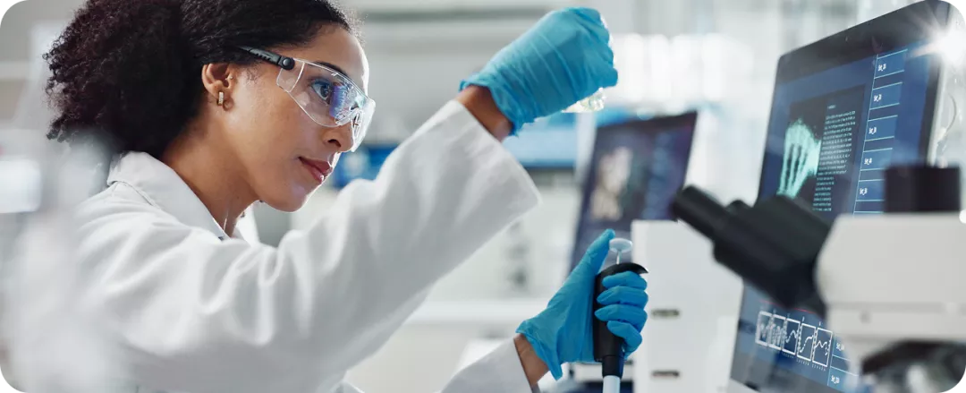 Mujer con bata de laboratorio trabajando en una computadora en un entorno de investigación.